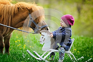 Little baby girl on wooden rocking horse and pony