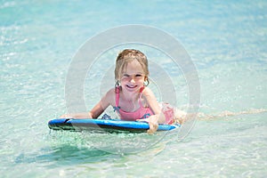 Little baby girl - young surfer with bodyboard has a fun on small ocean waves. Active family lifestyle.