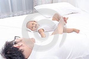 Little baby infant girl laying on white bed smiling to her daddy. Family having a happy time together