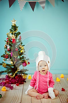 Little baby in knit winter clothing with knitted beanie and Decorating Christmas tree on green background