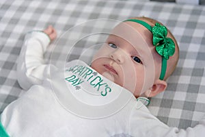 little baby laying in crib wearing st patricks day outfit an headband