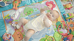 Little baby lying back on colorful carpet with toys. Infant boy portrait