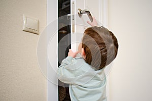 Little baby opens the door. Child pulls the door handle with the lock clo