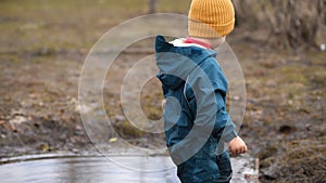 Little baby in overalls plays in a puddle and pulls out leaves and sticks