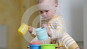 Little baby playing with educational colorful toys at home sitting on floor. Child having fun girl makes pyramid. Early
