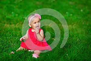 A little baby in a red dress sits on a grass