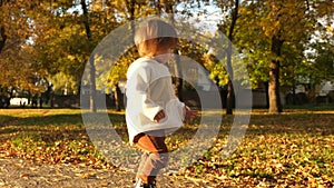 Little baby running around autumn park, laughing and playing with autumn leaves