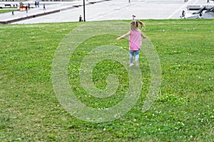 Little baby running on the grass against the background of a modern city