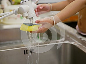 Little baby`s hand holding dishwashing sponge soaking in water, as she was washing kitchen sink by herself photo