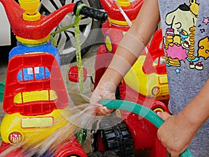 Little baby`s hands playing water and learning to wash plastic big bikes