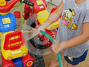 Little baby`s hands playing water and learning to wash plastic big bikes