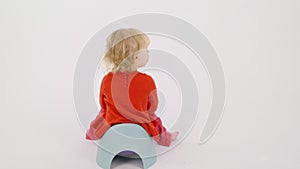 Little baby sits back on children's potty on isolated white background, peeing