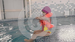 a little baby is sitting on the edge of the pool in a life jacket and with a trainer's whistle around her neck