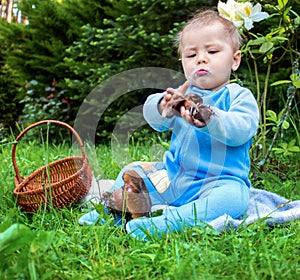 Little baby sitting on the grass in park and looking studied on mushroom