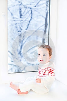 Little baby sitting at window to snowy garden