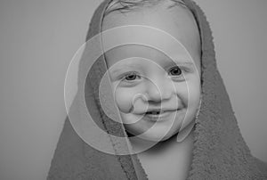 Little baby smiling under a white towel. Smiling baby boy bathing under a shower at home. Happy bath time.