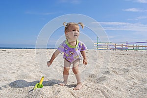 Little baby with two ponytails is standing in sand