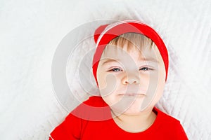 Little baby wearing Christmas clothes squints his eyes and smiles ridiculously. Close up portrait of a child with