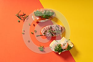 Little baguette sandwiches on vibrant yellow and orange background decorated with greens