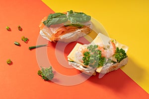 Little baguette sandwiches on vibrant yellow and orange background decorated with greens