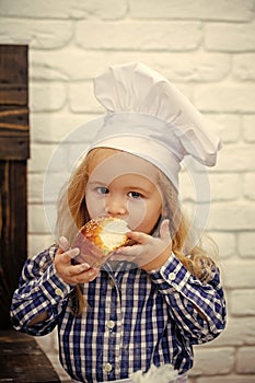 Little baker. Child eating bread bun on white brick wall