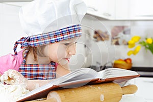 Little baker in hat preparing cookies with cookbook