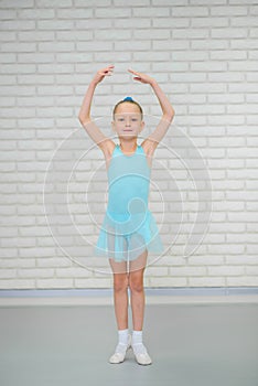 Little ballerina in blue dress and pointe shoes is dancing in ballet school. Cute girl in dance class.