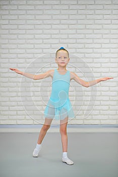 Little ballerina in blue dress and pointe shoes is dancing in ballet school. Cute girl in dance class.