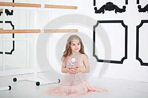 A little ballerina in a dress sits in a dance class on the floor. Little girl holding a musical toy carousel. The child receives a