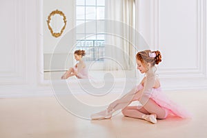 Little ballerina girl in a pink tutu and pointe shoes posing in white studio