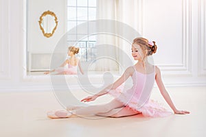 Little ballerina girl in a pink tutu and pointe shoes posing in white studio