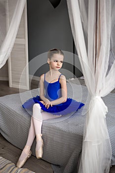 Little ballerina sitting on a bed. Cute little girl dreams of becoming a ballerina.