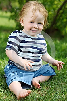 Little barefoot boy in shorts sitting on green