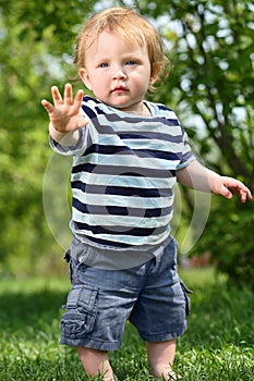 Little barefoot boy in shorts stands on green