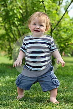 Little barefoot boy in striped T-shirt stands on