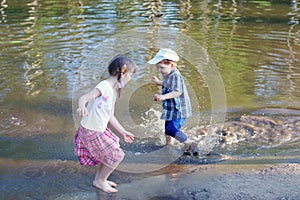 Little barefoot girl with boy laugh and run in water of pond