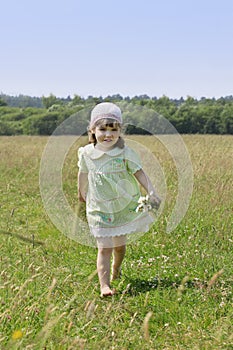 Little barefoot girl with flowers runs among grass