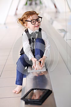 Little barefoot girl in glasses sits on floor in