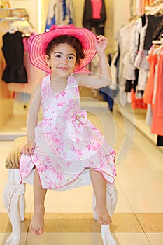 Little barefoot girl in hat sits in children store