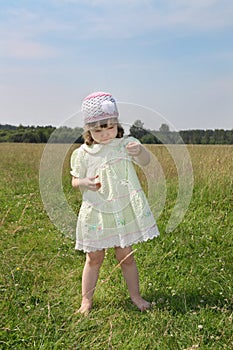 Little barefoot girl plays with camomile at green meadow