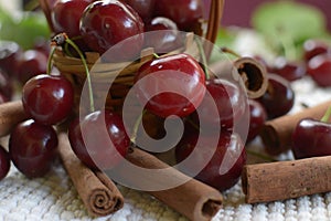 Little basket with handle, red cherries cinnamon rods on white