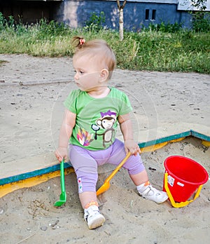 Little beautiful baby girl child plays bucket, rake and shovel in the sandbox sand