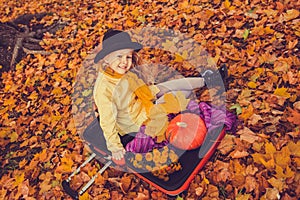Little beautiful blond girl with big pumpkin in autumn background