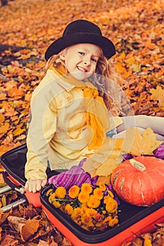 Little beautiful blond girl with big pumpkin in autumn background