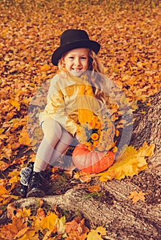 Little beautiful blond girl with big pumpkin in autumn background