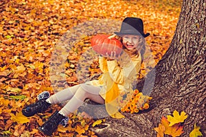 Little beautiful blond girl with big pumpkin in autumn background