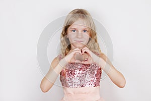 Little beautiful blond girl making heart shape with hands.