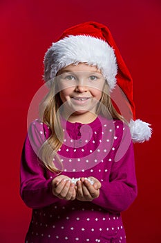 Little beautiful blond girl in red Santa hat holding snow.