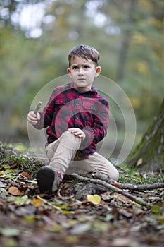Little beautiful boy sitting on the ground in a forest hurt