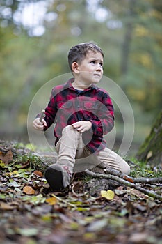 Little beautiful boy sitting on the ground in a forest hurt